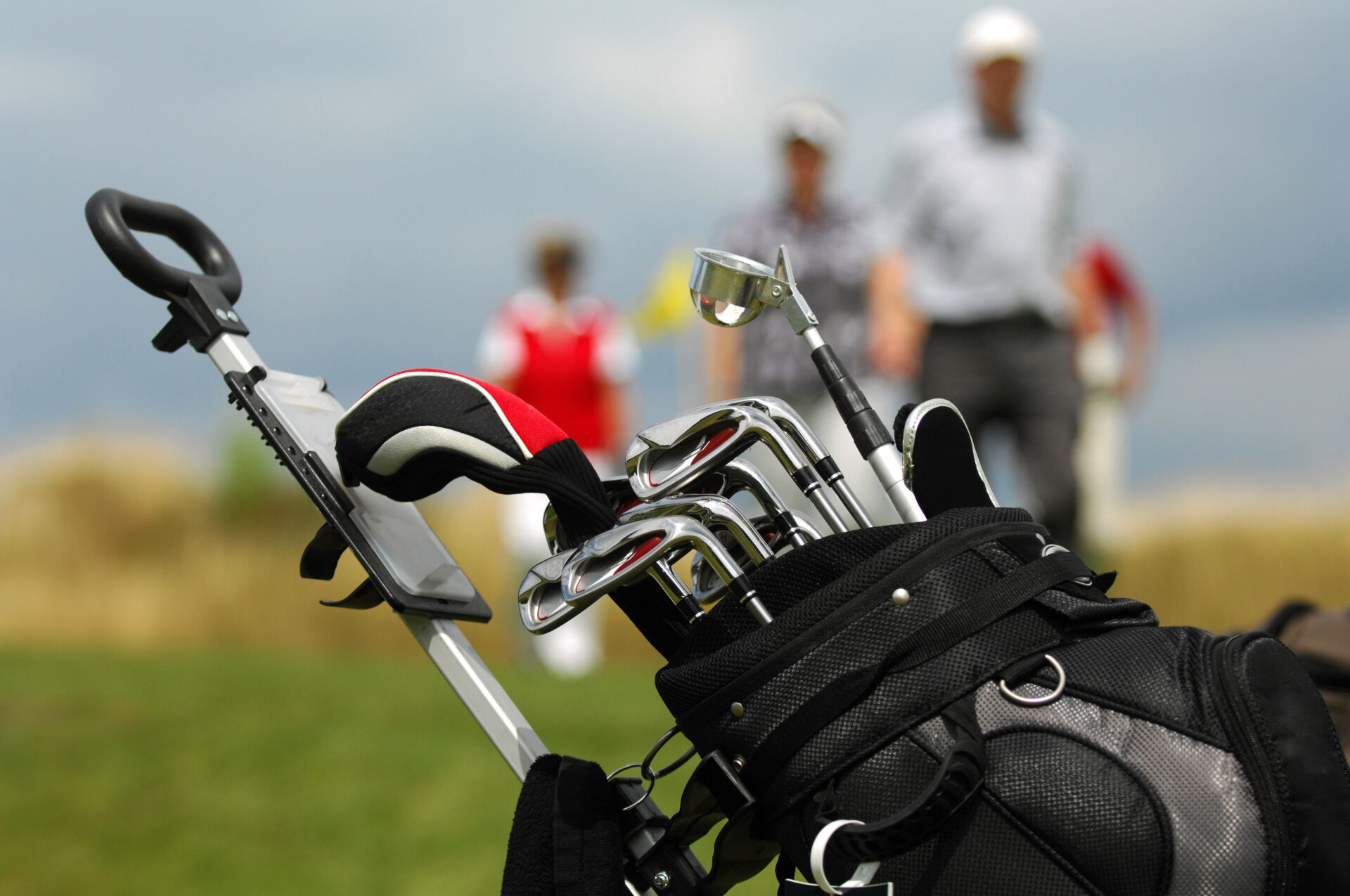 Eine Golftasche mit Schlägern steht im Vordergrund, unscharf im Hintergrund sind Golfer  zu sehen.